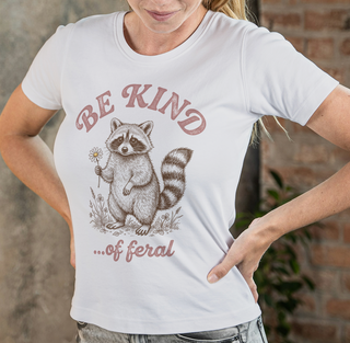 Person wearing a white t-shirt with a raccoon graphic and 'Be Kind...of feral' text.