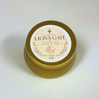 A round gold metal tin candle with a white circular label reading 'LION'S GATE' and featuring a lion illustration, photographed on a plain light background.