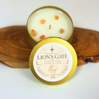 An open round candle tin with cream-colored wax and small orange stone accents sits behind a matching closed lid labeled 'LION'S GATE' on a wooden slice against a white background.