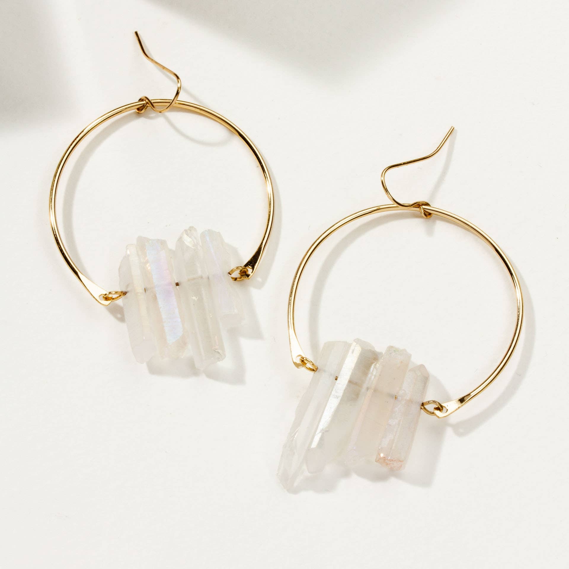 Gold hoop earrings with white stone accents on a light background