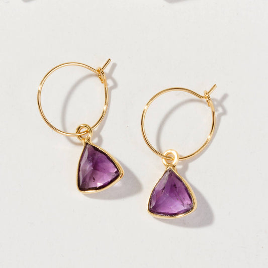 Gold hoop earrings with purple triangular gemstones on a white background