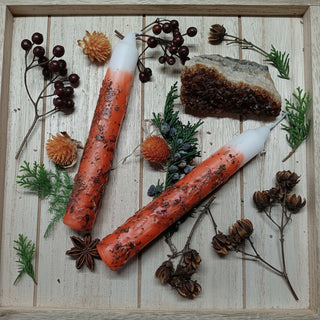 Two orange candles with white wicks on a wooden surface with decorative elements.