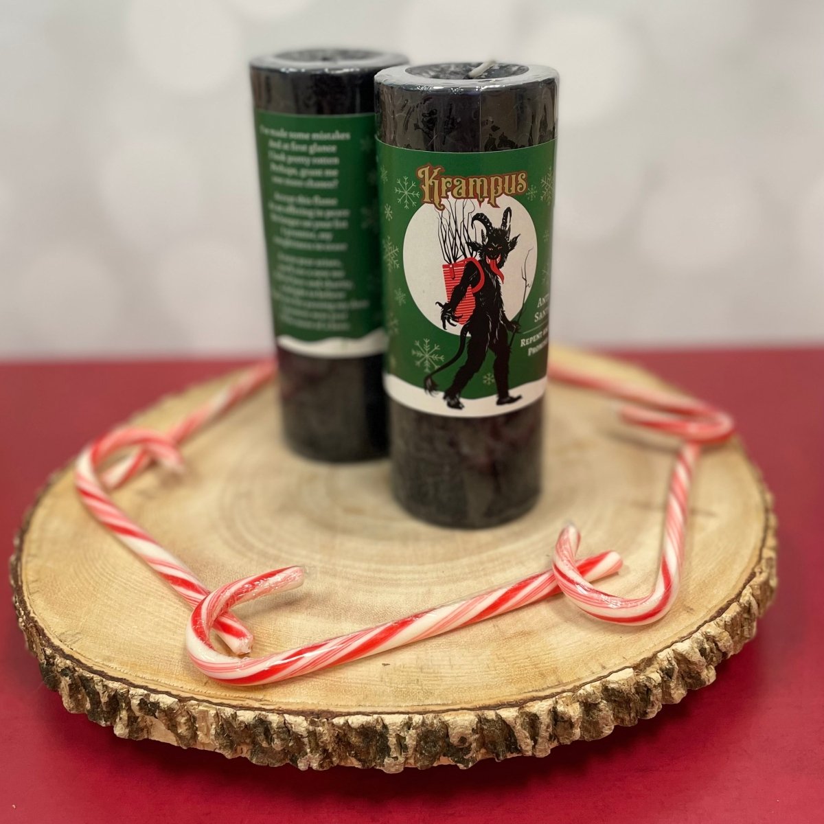 Two candles with Krampus design on labels on a wooden stand with candy canes.