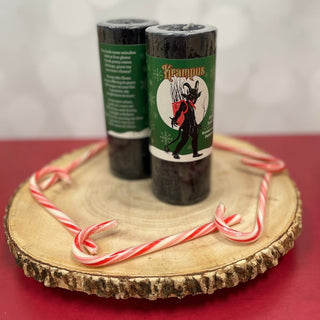 Two candles with Krampus design on labels on a wooden stand with candy canes.