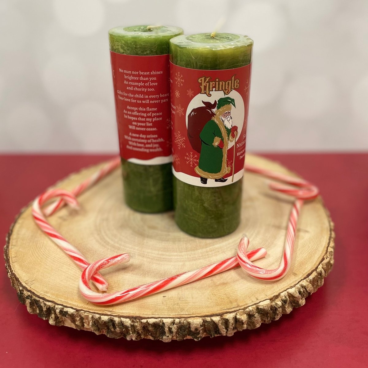 Two green candles with red labels on a wooden board with candy canes.