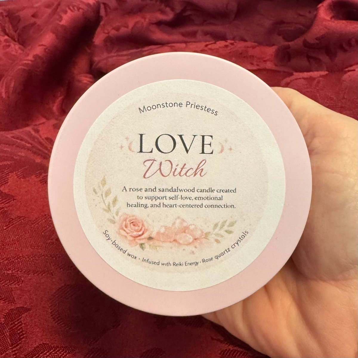 Candle packaging with 'Love Witch' branding on a red fabric background