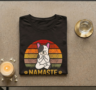 Dark grey heather Namaste Home With My Dog t-shirt folded on a textured surface with a candle and glass
