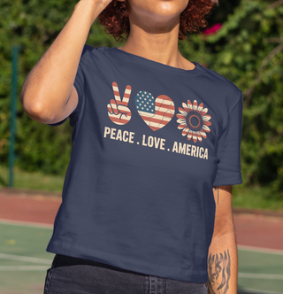 Person wearing a navy blue t-shirt with 'Peace Love America' design outdoors.