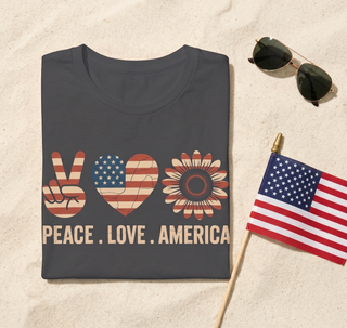 Gray t-shirt with 'Peace Love America' design on sand with sunglasses and small American flag.