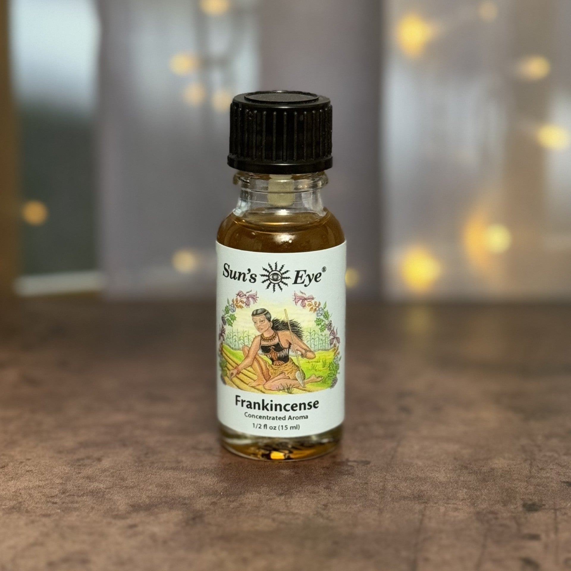 Bottle of Sun's Eye Frankincense concentrated aroma on a wooden surface with blurred lights in the background.