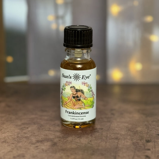 Bottle of Sun's Eye Frankincense concentrated aroma on a wooden surface with blurred lights in the background.