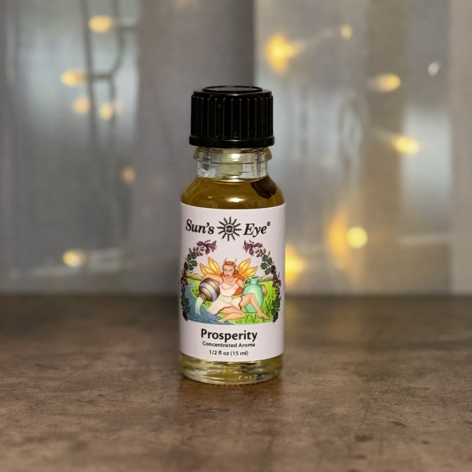 Bottle of Sun's Eye Prosperity concentrated aroma on a wooden surface with blurred lights in the background