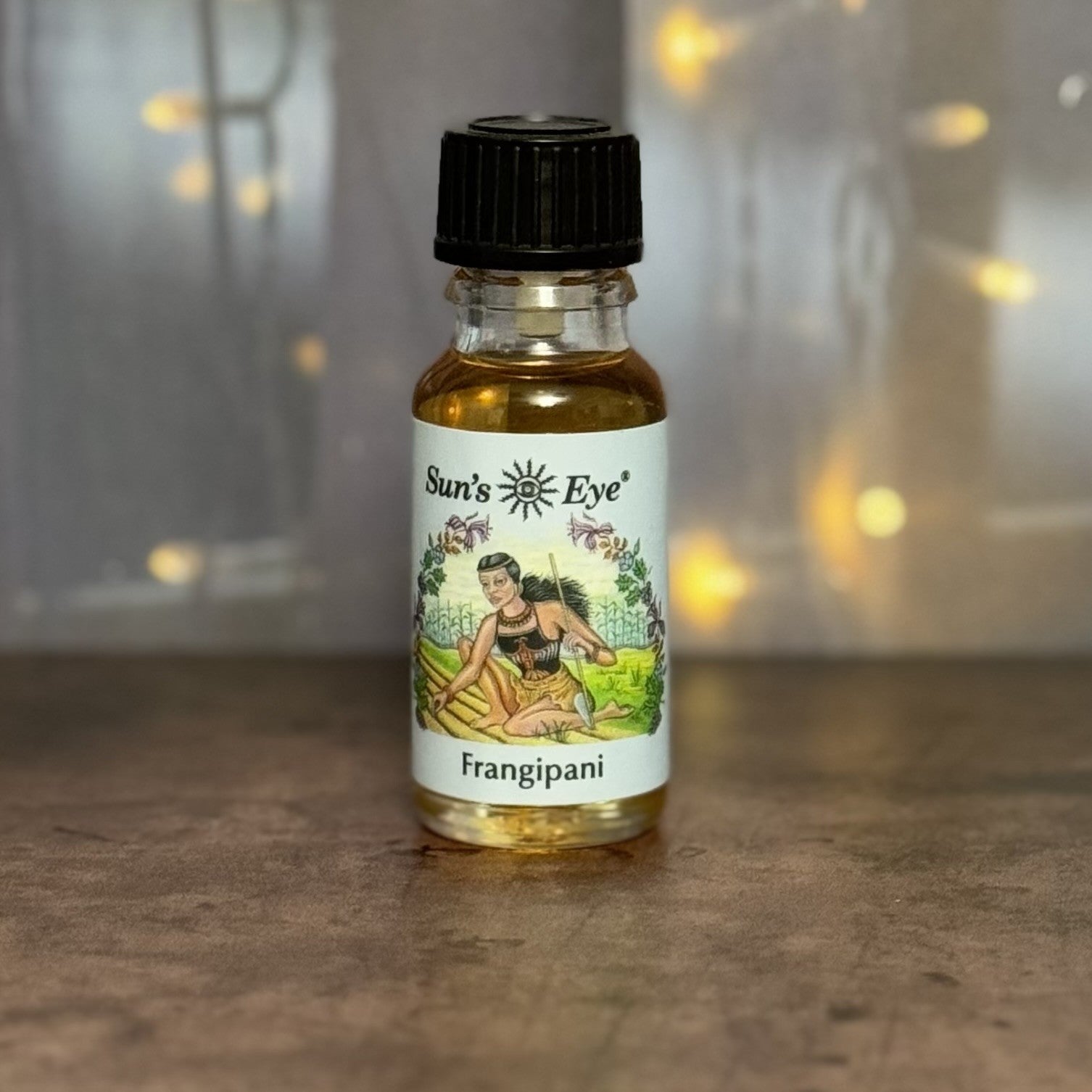 Small bottle of Sun's Eye Frangipani oil on a wooden surface with a blurred background