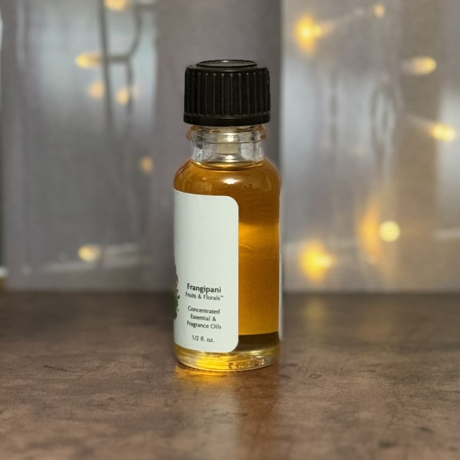 Small bottle of Frangipani fragrance oil with a black cap on a wooden surface.