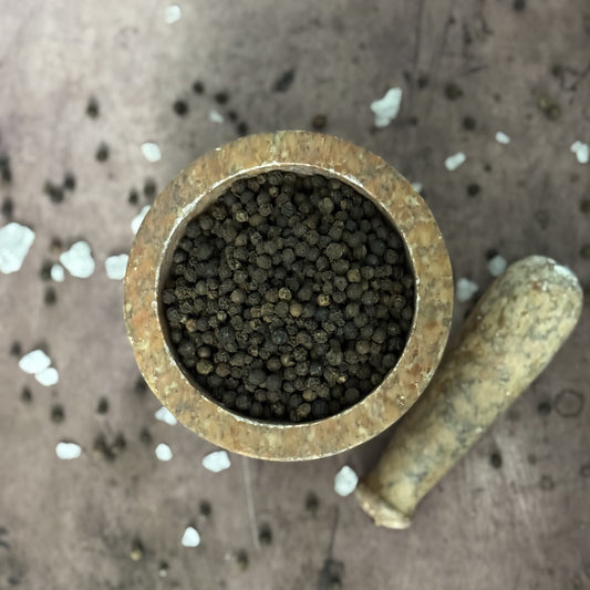 Brass container filled with small black peppercorn on a textured surface