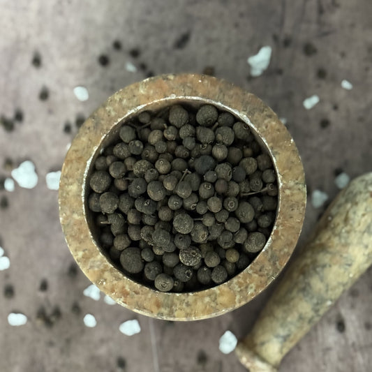 Close-up of a brass tube filled with small allspice on a textured surface.