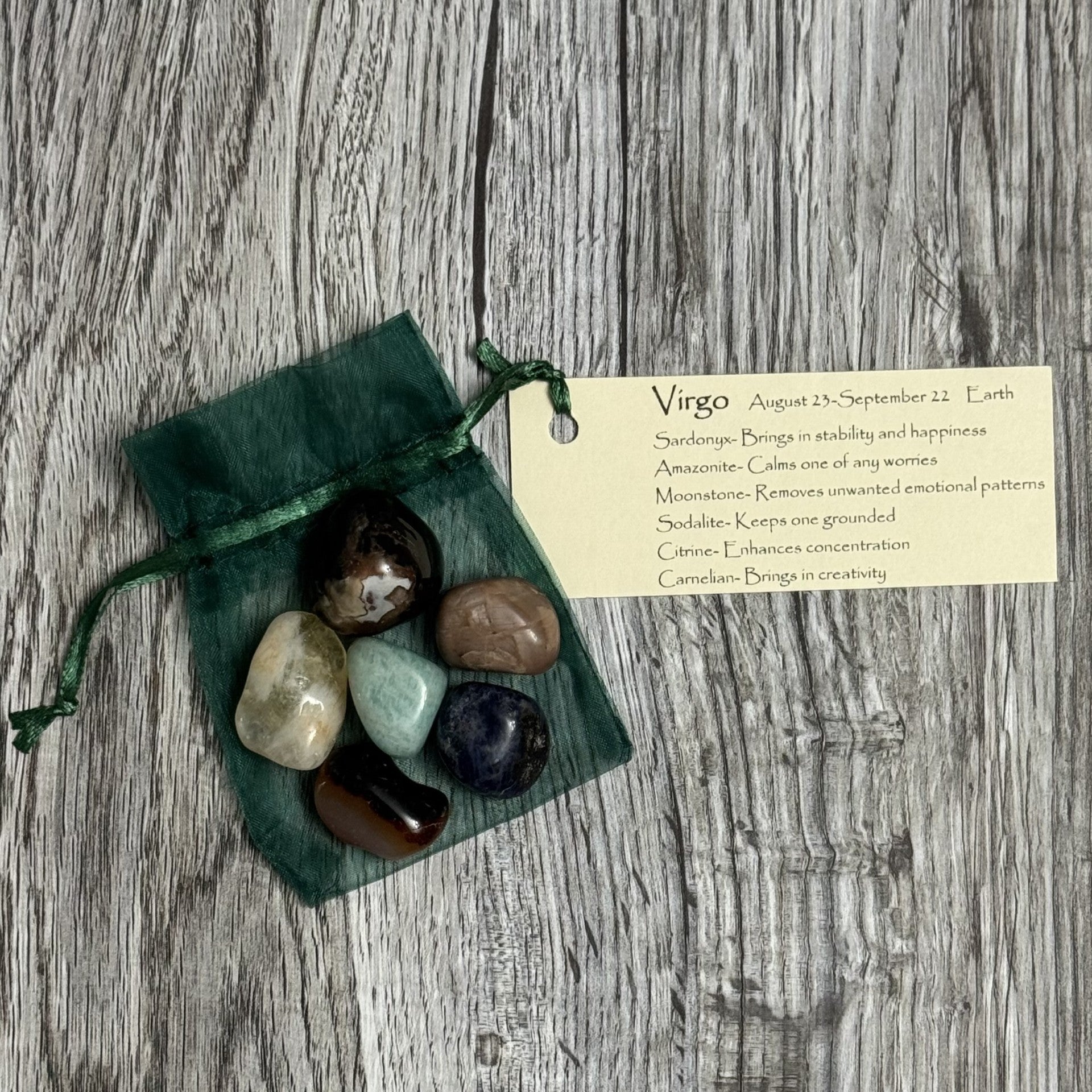 Set of tumbled stones in a green drawstring bag with a card on a wooden surface