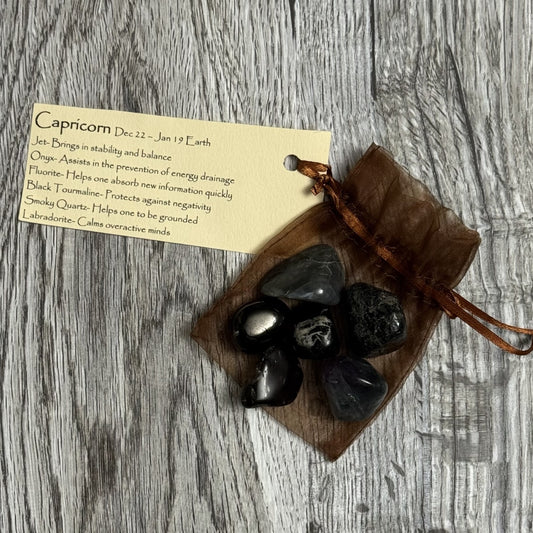 Black stones in a brown drawstring bag with a card on a wooden surface