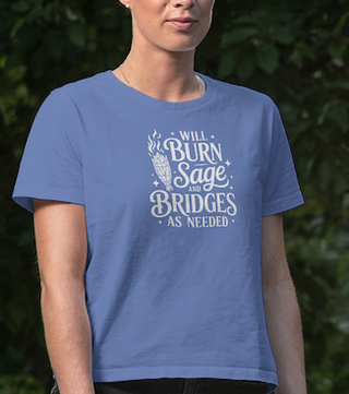 Person wearing a Heather True Royal blue 'Will burn sage and bridges' tee against a blurred green forest background
