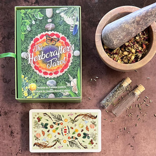 The image shows the Herbcrafter's Tarot deck and guidebook, with the deck laid out next to herbal ingredients and a mortar and pestle.